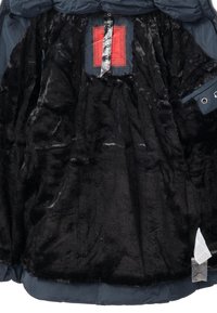 Zwarte nepbont binnenvoering van een jas met een rood label en hangtag, met een gladde buitenstof en een omgeslagen zoom aan de onderkant.