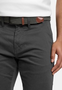 Grijze katoenen broek met een geweven zwarte en crèmekleurige riem. De riem heeft bruine leren accenten, die een textuurrijke detail aan de outfit toevoegen.