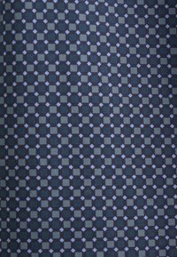 Tessuto tessile con un motivo geometrico di quadrati blu navy alternati a rombi grigio chiaro su uno sfondo scuro.