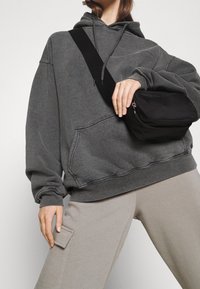 Felpa grigia oversize con tasca frontale, abbinata a pantaloni della tuta beige con tasca laterale. Borsa a tracolla nera con chiusura a zip.