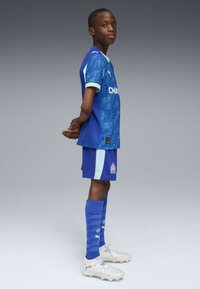 Zils futbola tērps ar rakstainu kreklu, gaiši ziliem akcentiem, atbilstošām biksēm un ziliem strukturētiem zeķēm. Sudraba zābaki pievieno detaļu.