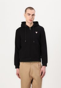 Camisola com fecho éclair preta, com capuz ajustável e um pequeno logótipo triangular no peito. Feita de um tecido macio com punhos canelados.