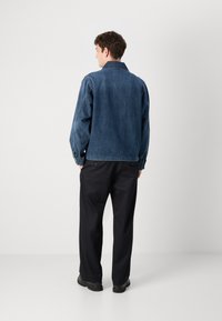 Jachetă din denim de culoare albastru închis, cu un croi lejer, mansete cu nasturi și guler. Purtați peste pantaloni negri și pantofi negri rezistenți.