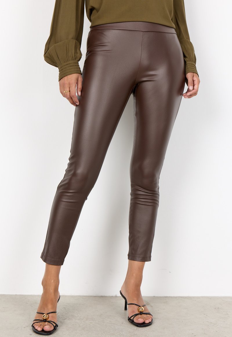 Brown faux leather leggings with a fitted design, smooth texture, and ankle-length cut. Paired with black strappy heels.