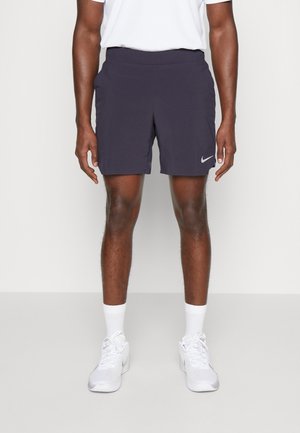 Pantalones cortos para hombre de Nike en gris oscuro, tela ligera, cintura elástica, bolsillos laterales, textura suave, combinados con zapatillas y calcetines blancos.