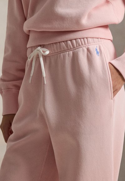 Ροζ ανοιχτόχρωμο παντελόνι φόρμας από απαλό ύφασμα, με ελαστική μέση και λευκό κορδόνι, καθώς και μικρό μπλε λογότυπο στην πλαϊνή τσέπη.
