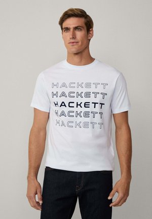 White short-sleeve t-shirt with black "HACKETT" text printed repeatedly in various fonts. Made of cotton with a smooth texture.