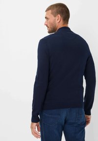 Marineblå strikket sweater med langeærmer, ribmede manchetter og kant, glat tekstur og rund halsudskæring. Sammen med blå denimjeans.