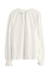 Hvid langærmet bluse med et tekstureret diamantmønster, rund halsudskæring, knaplukning bagpå og samlede manchetter.