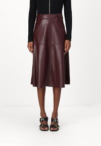 Jupe midi en cuir bordeaux avec un design évasé, poches avant plates et texture lisse, assortie à des sandales à lanières noires.