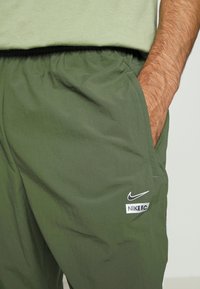 Grüne, leichte Sporthose mit elastischem Bund. Verfügt über eine Seitentasche und ein aufgedrucktes weißes Nike-Logo sowie das Nike F.C.-Label.