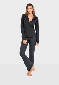 Crni sportski set koji uključuje jaknu na zip s ovratnikom i dugim rukavima, u kombinaciji s tajicama koje dobro prijanjaju, izrađen od glatkog, rastezljivog materijala.