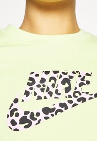 Světle zelené tričko s velkým logem Nike, které má design růžového leopardího vzoru. Kulatý výstřih a texturovaná bavlněná tkanina.