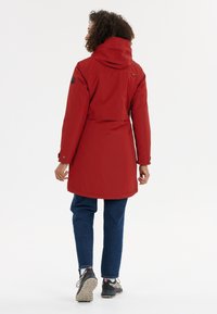 Punainen vedenpitävä parka hupulla, joustavilla hihansuilla ja vyöllä. Ominaisuuksiin kuuluu keskipitkä muotoilu ja sileä, mattapintainen tekstuuri.