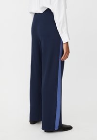 Granatowe spodnie o szerokich nogawkach z niebieskim paskiem po bokach, wykonane z gładkiej, lekkiej tkaniny. Posiadają elastyczną talię dla komfortu.