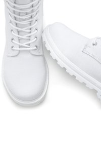 Chaussures blanches à lacets avec un dessus en toile, bout rond et semelle en caoutchouc texturé. Présentent des œillets métalliques et des détails de couture contrastants.