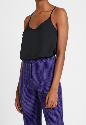 Camisola in satin nero con spalline sottili abbinata a pantaloni a vita alta con motivo houndstooth viola, dotati di chiusura con zip laterale.