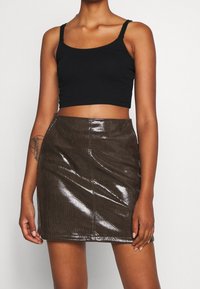 Débardeur noir court associé à une mini-jupe marron foncé brillante avec une texture en maille et des coutures visibles.