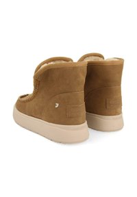 Bottes ankle en daim marron avec un intérieur douillet, présentant une forme arrondie, une texture douce et une semelle extérieure crème. Inclut un accent de logo simple.