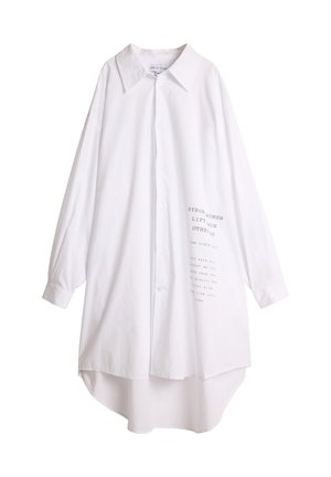 Hvit skjorte med krage, lange ermer og høy-lav hem. Har trykt tekst foran i grått. Myk stofftekstur.
