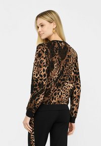 Felpa con stampa leopardata in marrone e nero, dotata di polsini e orlo a coste, texture morbida e vestibilità comoda, abbinata a pantaloni neri.