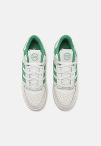 White sneakers with green stripes, perforated toe area, padded collar, and white laces. Circular logo on tongue. Flat rubber sole.
