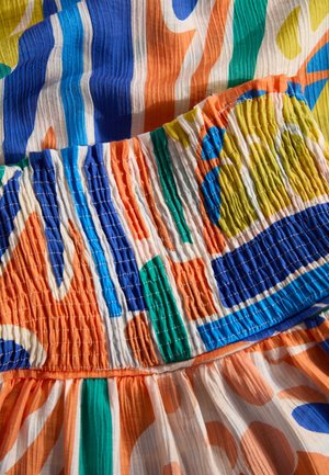Robe colorée avec un corsage smocké, présentant des motifs ondulés en bleu, orange, vert, jaune et tissu froissé blanc.