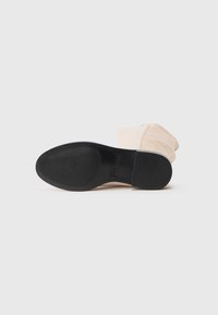 Beige ankelstøvle med en tekstureret overdel, rund tå og en sort gummisål med ribbet mønster for bedre greb. Ingen synlige hardware eller accenter.