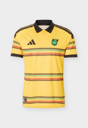 Κίτρινη φανέλα ποδοσφαίρου της Τζαμάικα με μαύρο γιακά, πολύχρωμες οριζόντιες ρίγες, το λογότυπο της Adidas στο δεξί στήθος και το έμβλημα της Ποδοσφαιρικής Ομοσπονδίας της Τζαμάικας αριστερά.