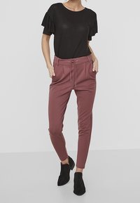 Haut noir à manches courtes avec des manches volantes, associé à un pantalon bordeaux ajusté avec une taille à cordon et des poches avant, porté avec des bottines noires.