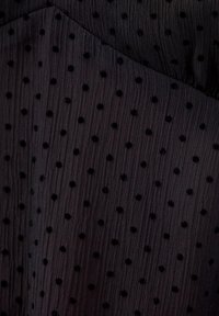 Musta tekstuurikangas, jossa on pieniä kohotettuja samettipolkka-pisteitä tasaisesti sijoiteltuna, näyttäen taitoksilta ja hienovaraiselta kiillolta.