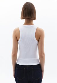 Vit ribbad ärmless topp med en figurnära silhuett och breda band. Kombinerad med mörkblå jeans med kontrasterande sömmar.