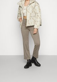 Pufferjacka i beige med stort logotryck, i kombination med brun rutiga byxor och svarta anklar stövlar med kraftig sula.