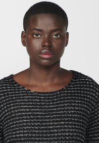 Maglione nero in maglia testurizzata con una vestibilità ampia e una scollatura larga. Presenta filati opachi e lucidi alternati creando un motivo a righe.