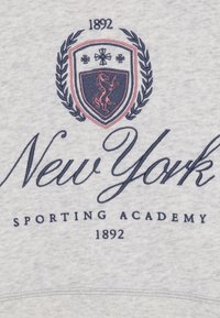 Hellgrauer Pullover mit navyblauem Text, der "New York Sporting Academy" und ein Wappen mit einem Pferd zeigt. Das bemerkenswerte Jahr "1892" ist ebenfalls enthalten.