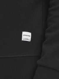 Black sweatshirt featuring a small white label with brand name and text. Material is soft with a smooth texture and ribbed cuff detail.