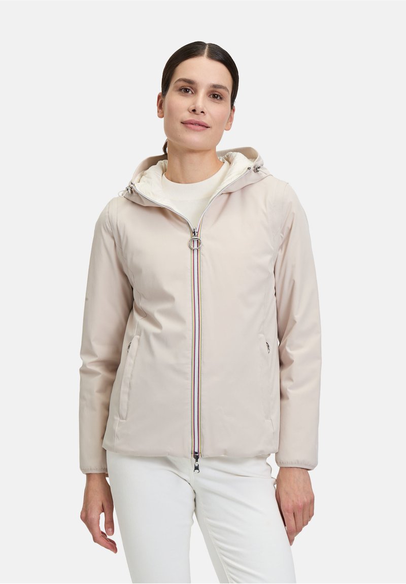 Veste à capuche beige clair avec fermeture éclair à l'avant, fermeture éclair à accent coloré et deux poches latérales. Tissu lisse avec une doublure intérieure douce.