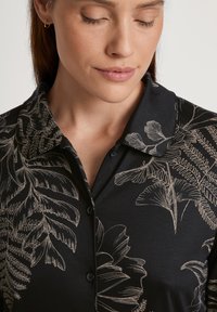 Zwart shirt met een kraag, voorzien van een botanisch patroon in beige. Het materiaal lijkt soepel met knopen en delicate bladmotieven.