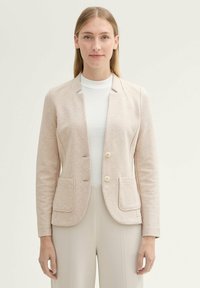 Veste beige clair avec une texture lisse, deux boutons et deux poches avant. Comprend un design ajusté et une silhouette légèrement cintrée.