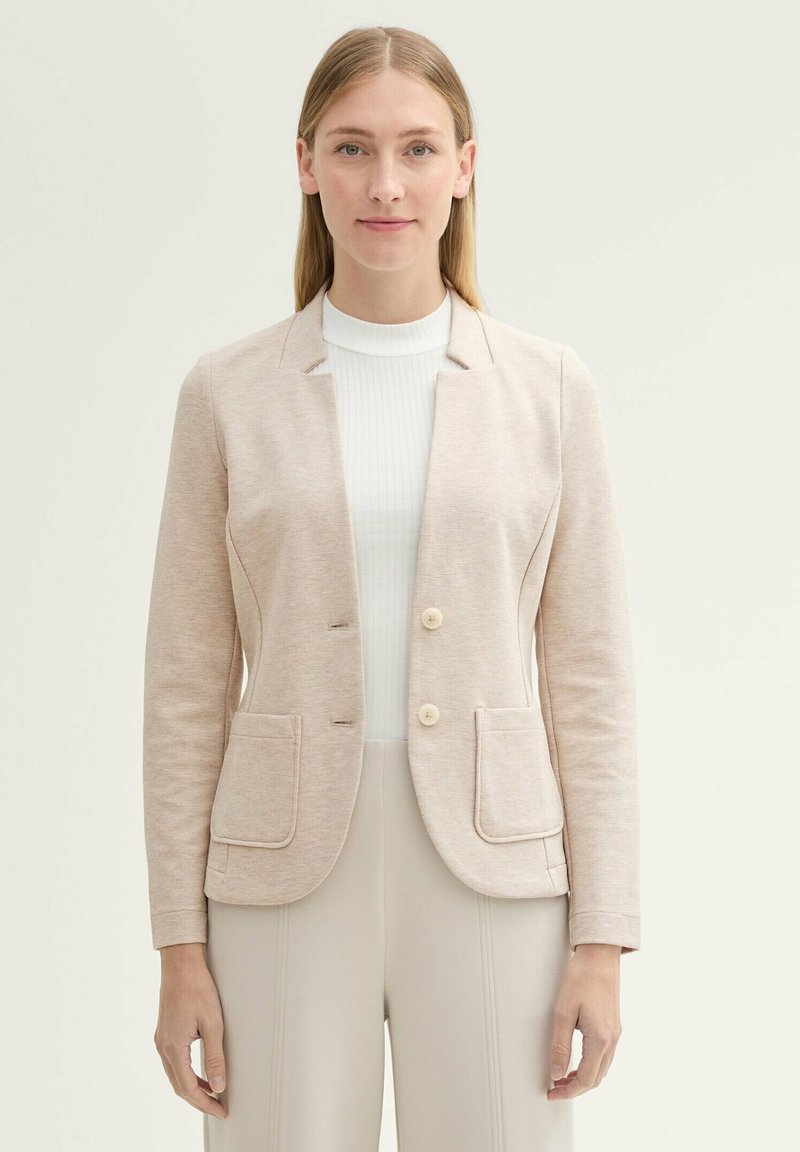 Veste beige clair avec une texture lisse, deux boutons et deux poches avant. Comprend un design ajusté et une silhouette légèrement cintrée.