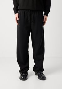 Zwarte sweatpants met een elastische tailleband en verstelbaar trekkoord. Voorzien van zijzakken en een gestructureerde zwarte logopatch op de bovenbeen.