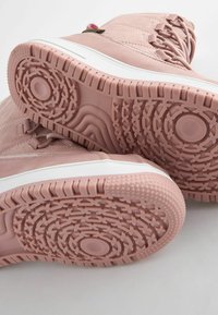 Rosa Wildleder-Stiefeletten mit weißen Gummisohlen, die über strukturierte Profilmuster und Schnürdetails für einen sicheren Sitz verfügen.
