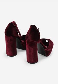 Tacones de plataforma de terciopelo burdeos con gruesos tacones cuadrados, punta redonda y correa en el tobillo, que presentan una textura suave y una silueta elegante.