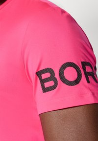 Rosa, kortermet skjorte med en glatt tekstur og svart prikket skrift som leser "BOR" på ermet. Slim fit design.