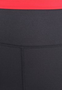 Legging de sport noirs avec une texture lisse et une large ceinture rouge. Comprend des coutures renforcées le long des seams pour plus de durabilité.