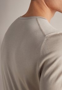 Jasnoszara, dopasowana koszulka z okrągłym dekoltem, gładka w dotyku, z subtelnym detalem przeszycia, ukazująca widok z tyłu na ramionach.