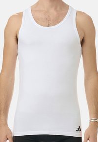 Vit ärmlös linne i mjukt bomullsmaterial. Har en rund halsringning och en liten svart logotyp i det nedre vänstra hörnet.