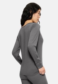 Długi rękaw sportowej bluzki w szarym kolorze. Posiada okrągły dekolt, gładką teksturę, dopasowany krój i wykończenie szwów.