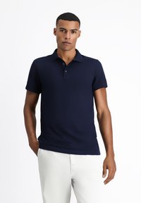 Granatowa koszulka polo wykonana z gładkiego, przewiewnego materiału; posiada kołnierzyk, krótkie rękawy i zapięcie na trzy guziki.