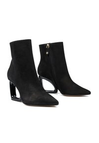 Czarne zamszowe botki do kostek z ostrymi noskami, unikalnymi wklęsłymi podkówkowymi obcasami oraz bocznymi zamkami błyskawicznymi z małymi złotymi uchwytami.